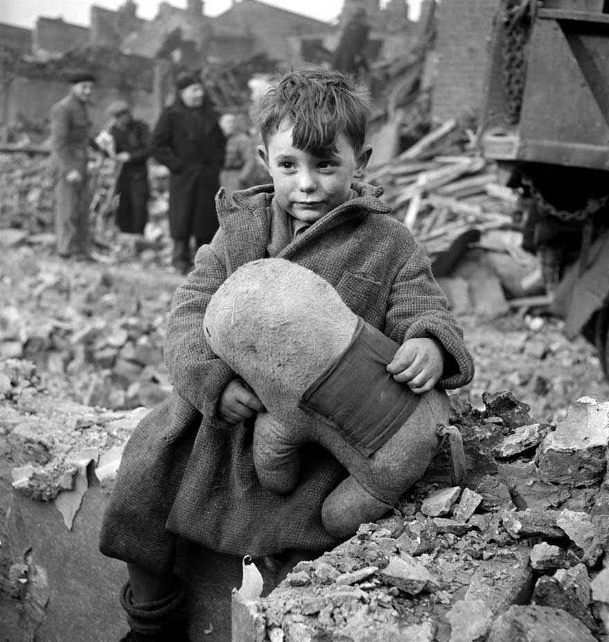 A black and white antique photo of a boy in rubble before colorization